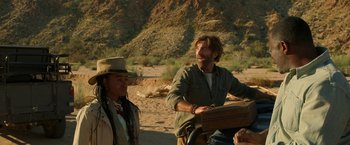 Movie still from “Beast” (2022), directed by Baltasar Kormákur – A man standing next to another man on a dirt road; Medium shot, Over the shoulder angle