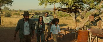 Movie still from “Beast” (2022), directed by Baltasar Kormákur – A group of people standing next to each other on a dirt road; Medium shot, Over the shoulder angle