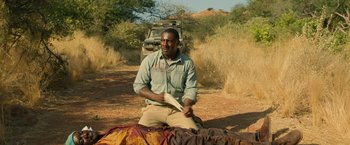 Movie still from “Beast” (2022), directed by Baltasar Kormákur – A man sitting on top of a dirt field; Medium shot, Over the shoulder angle