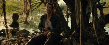 Movie still from “Beast” (2022), directed by Baltasar Kormákur – A man sitting on the ground next to a body of water; Medium shot, Low angle