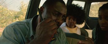 Movie still from “Beast” (2022), directed by Baltasar Kormákur – A man sitting in the back seat of a car talking on a cell phone; Close Up shot, Over the shoulder angle