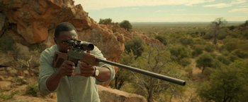 Movie still from “Beast” (2022), directed by Baltasar Kormákur – A man is holding a rifle in his hand; Medium shot, Over the shoulder angle