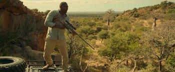 Movie still from “Beast” (2022), directed by Baltasar Kormákur – A man holding a rifle while standing on top of a platform; Wide shot, Low angle