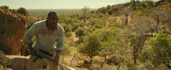 Movie still from “Beast” (2022), directed by Baltasar Kormákur – A man standing on top of a tree in the middle of a forest; Medium shot, Low angle