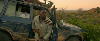 Movie still from “Beast” (2022), directed by Baltasar Kormákur – A man holding a wooden stick in front of a truck; Medium shot, Over the shoulder angle
