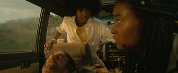 Movie still from “Beast” (2022), directed by Baltasar Kormákur – A woman standing next to a man laying in a car; Medium shot, Over the shoulder angle