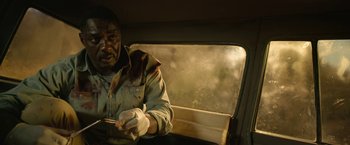 Movie still from “Beast” (2022), directed by Baltasar Kormákur – A man sitting in a vehicle holding a cigarette; Close Up shot, High angle