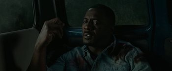 Movie still from “Beast” (2022), directed by Baltasar Kormákur – A man sitting on a train with his hand on his chest; Close Up shot, High angle