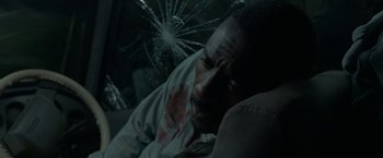 Movie still from “Beast” (2022), directed by Baltasar Kormákur – A man laying on a couch with a broken window behind him; Close Up shot, High angle