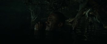 Movie still from “Beast” (2022), directed by Baltasar Kormákur – A man in a dark room with trees in the background; Close Up shot, High angle