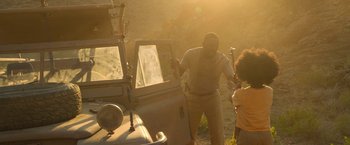 Movie still from “Beast” (2022), directed by Baltasar Kormákur – A man and a child are standing next to an old car; Medium shot, Over the shoulder angle