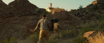 Movie still from “Beast” (2022), directed by Baltasar Kormákur – A group of people walking up a hill near a building; Wide shot, Low angle
