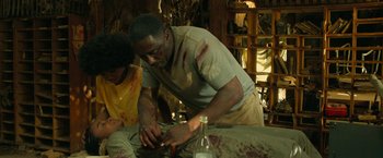 Movie still from “Beast” (2022), directed by Baltasar Kormákur – A man and a woman working on something in a room; Medium shot, High angle