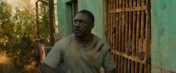 Movie still from “Beast” (2022), directed by Baltasar Kormákur – A man with a bruise on his face standing in front of a building; Medium shot, Low angle