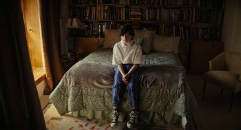 Movie still from “Beautiful Boy” (2018), directed by Felix van Groeningen – A person sitting on a bed in front of a book shelf; Wide shot, High angle