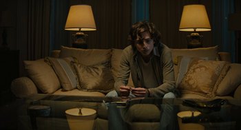 Movie still from “Beautiful Boy” (2018), directed by Felix van Groeningen – A man sitting on top of a couch looking at his phone; Medium shot, Low angle