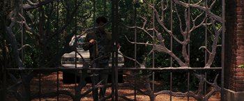 Movie still from “Beautiful Creatures” (2013), directed by Richard LaGravenese – A man standing behind a metal fence in a park; Wide shot, Over the shoulder angle