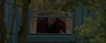 Movie still from “Becky” (2020), directed by Jonathan Milott – A man with a beard looking out of a window; Medium shot, Low angle
