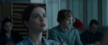 A young woman holding a flower in front of a young man