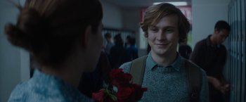 A young man holding a bouquet of red roses in front of another young man