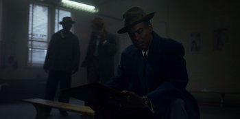 Movie still from “Fargo” (2014), created by Noah Hawley – A man wearing a hat is looking at a book; Medium shot, Low angle