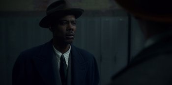Movie still from “Fargo” (2014), created by Noah Hawley – A man wearing a suit and a hat is standing in a dark room; Close Up shot, Over the shoulder angle