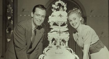 Movie still from “Beginners” (2010), directed by Mike Mills – A man and a woman standing in front of a wedding cake; Medium shot, Overhead angle