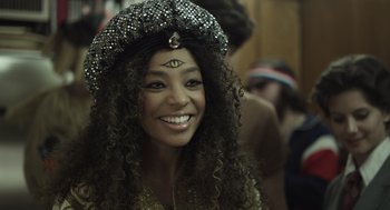 Movie still from “Beginners” (2010), directed by Mike Mills – A woman in a black hat and a gold dress smiling for the camera; Close Up shot, Over the shoulder angle