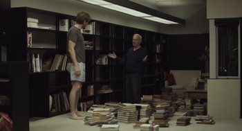 Movie still from “Beginners” (2010), directed by Mike Mills – Two men standing in a room full of stacks of books; Wide shot, High angle