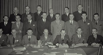Movie still from “Beginners” (2010), directed by Mike Mills – A group of men sitting at a table in front of a wall; Medium shot, High angle