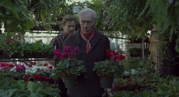 Movie still from “Beginners” (2010), directed by Mike Mills – A man holding two potted plants in a garden; Medium shot, Over the shoulder angle