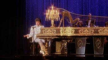 Movie still from “Behind the Candelabra” (2013), directed by Steven Soderbergh – A man sitting at a grand piano in front of a chandelier; Wide shot, High angle