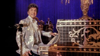 Movie still from “Behind the Candelabra” (2013), directed by Steven Soderbergh – A man in a sequined suit standing next to a piano; Medium shot, Low angle