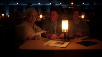 Movie still from “Behind the Candelabra” (2013), directed by Steven Soderbergh – A group of people sitting at a table with a lit candle; Medium shot, High angle