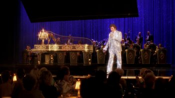 Movie still from “Behind the Candelabra” (2013), directed by Steven Soderbergh – A man in a white suit is on a stage; Wide shot, Over the shoulder angle