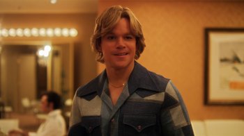 Movie still from “Behind the Candelabra” (2013), directed by Steven Soderbergh – A man with long blonde hair wearing a blue and white shirt; Medium shot, Over the shoulder angle