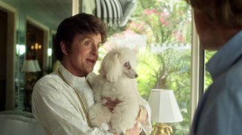 Movie still from “Behind the Candelabra” (2013), directed by Steven Soderbergh – A man holding a small white dog in his arms; Close Up shot, Over the shoulder angle