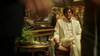 Movie still from “Behind the Candelabra” (2013), directed by Steven Soderbergh – A man in a white suit sitting in a chair in a room; Medium shot, Over the shoulder angle