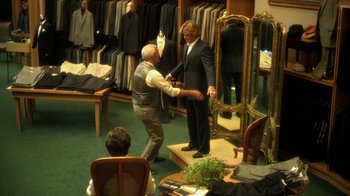 Movie still from “Behind the Candelabra” (2013), directed by Steven Soderbergh – A man in a suit and tie is trying on a suit in a suit shop; Wide shot, Over the shoulder angle