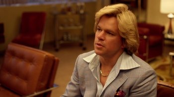 Movie still from “Behind the Candelabra” (2013), directed by Steven Soderbergh – A man with blonde hair sitting in front of a chair; Close Up shot, Over the shoulder angle