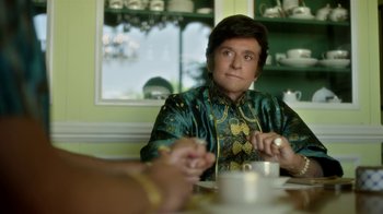 Movie still from “Behind the Candelabra” (2013), directed by Steven Soderbergh – A person sitting at a table with a plate of food; Medium shot, Over the shoulder angle