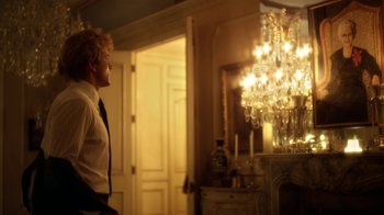 Movie still from “Behind the Candelabra” (2013), directed by Steven Soderbergh – A man standing in front of a chandelier in a room; Medium shot, Over the shoulder angle