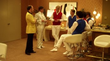 Movie still from “Behind the Candelabra” (2013), directed by Steven Soderbergh – A group of men standing around each other in a room; Wide shot, Over the shoulder angle