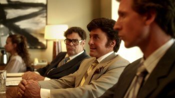 Movie still from “Behind the Candelabra” (2013), directed by Steven Soderbergh – A group of men in suits sitting next to each other in a room; Medium shot, Over the shoulder angle