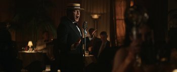 Movie still from “Being the Ricardos” (2021), directed by Aaron Sorkin – A man wearing a suit and hat singing into a microphone in front of other people; Medium shot, Low angle