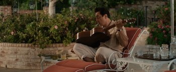 Movie still from “Being the Ricardos” (2021), directed by Aaron Sorkin – A man sitting on the ground holding a guitar; Medium shot, High angle