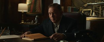 Movie still from “Being the Ricardos” (2021), directed by Aaron Sorkin – An older man sitting at a table looking at a book; Medium shot, Low angle