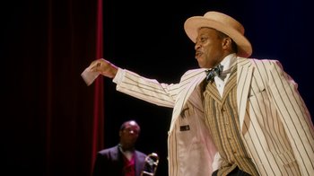 Movie still from “Bessie” (2015), directed by Dee Rees – A man wearing a straw hat and a striped jacket; Medium shot, Low angle