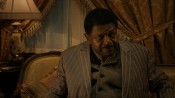 Movie still from “Bessie” (2015), directed by Dee Rees – A man in a suit and tie sitting on a couch; Close Up shot, High angle