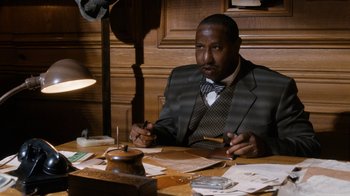 Movie still from “Bessie” (2015), directed by Dee Rees – A man sitting at a table in front of papers; Medium shot, Low angle